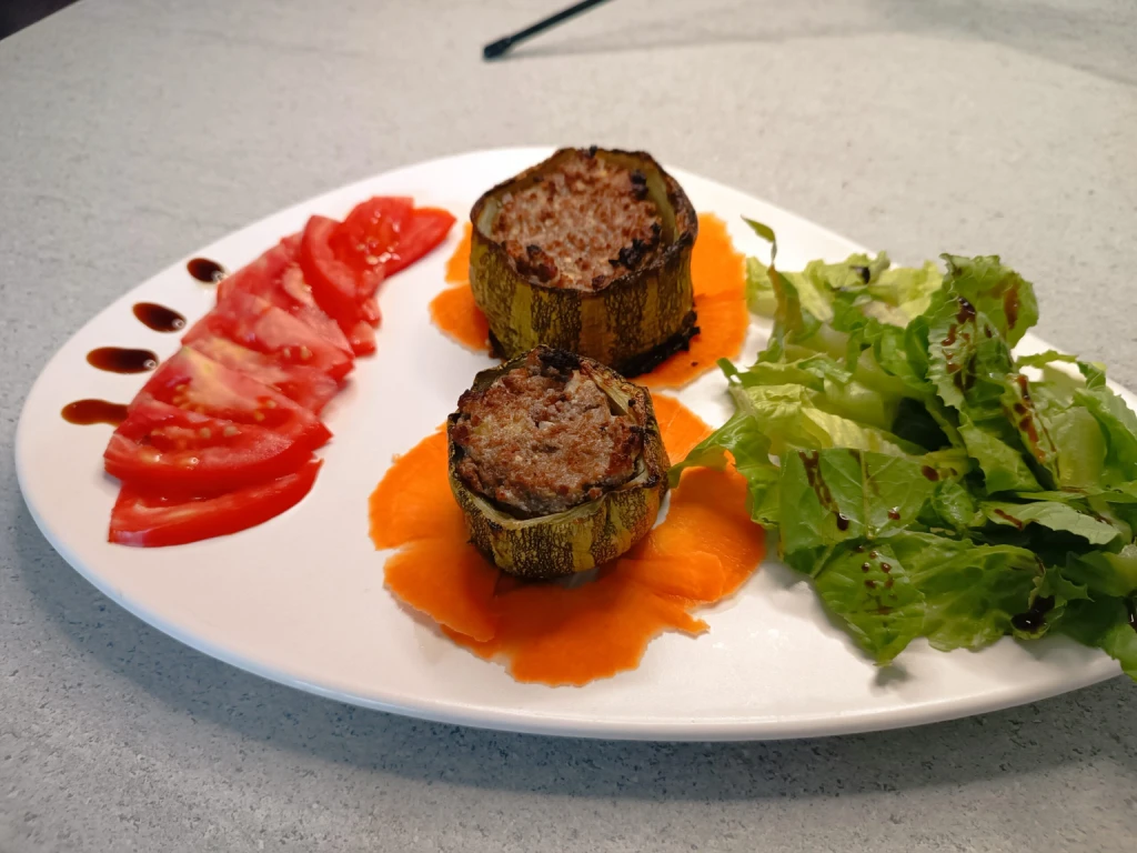 Calabacines rellenos servidos en un plato blanco con tomates picados y ensalada.