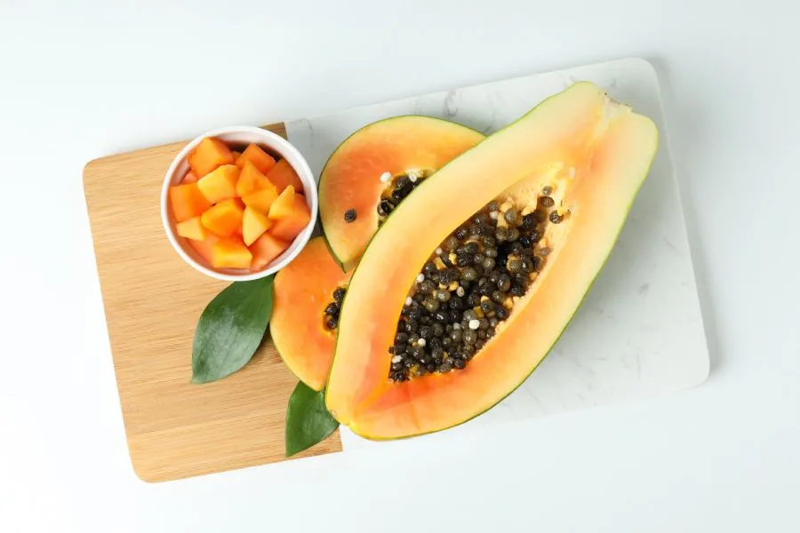 Imagen de una papaya cortada por la mitad colocada sobre una tabla de cortar.