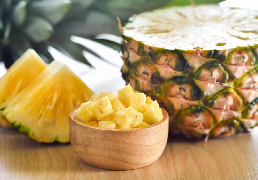 Imagen de una piña cortada en varios tamaños dispuesta sobre una mesa de madera.