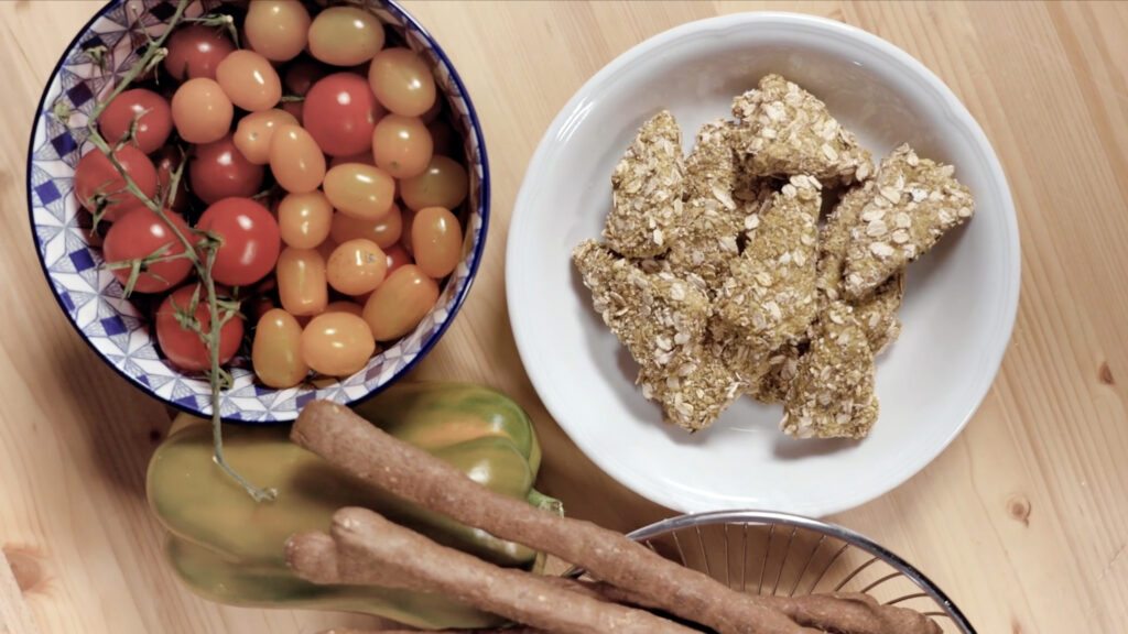 Nuggets de pollo empanados acompañados de tomates cherry, pimiento y pan, dispuestos sobre una mesa de madera.