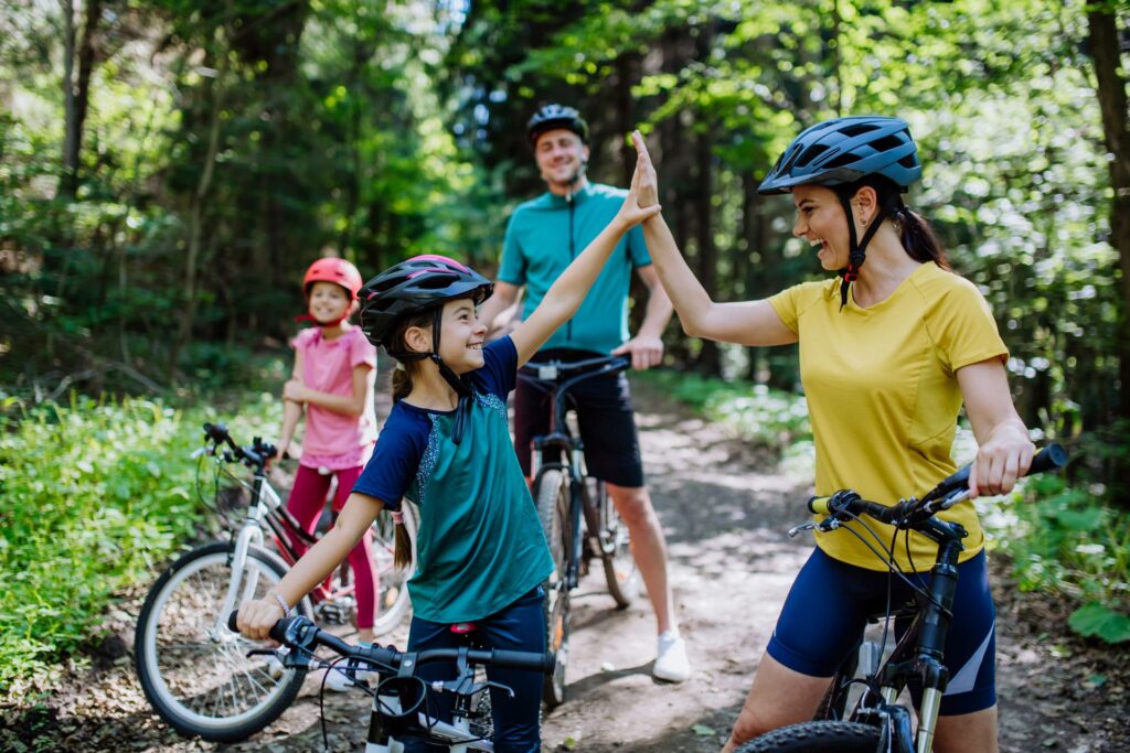 Familia montando en bicicleta por el bosque, sonriendo y chocando las manos durante una pausa en el camino.