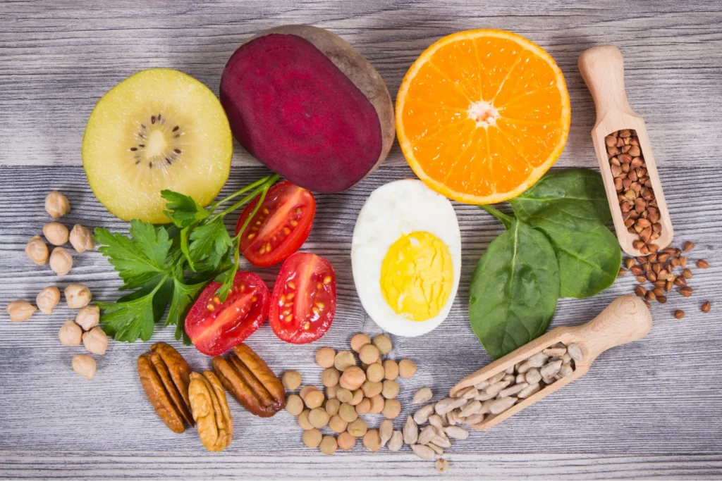 Variedad de alimentos saludables —como frutas, verduras, legumbres, frutos secos y huevo— dispuestos sobre una superficie de madera.