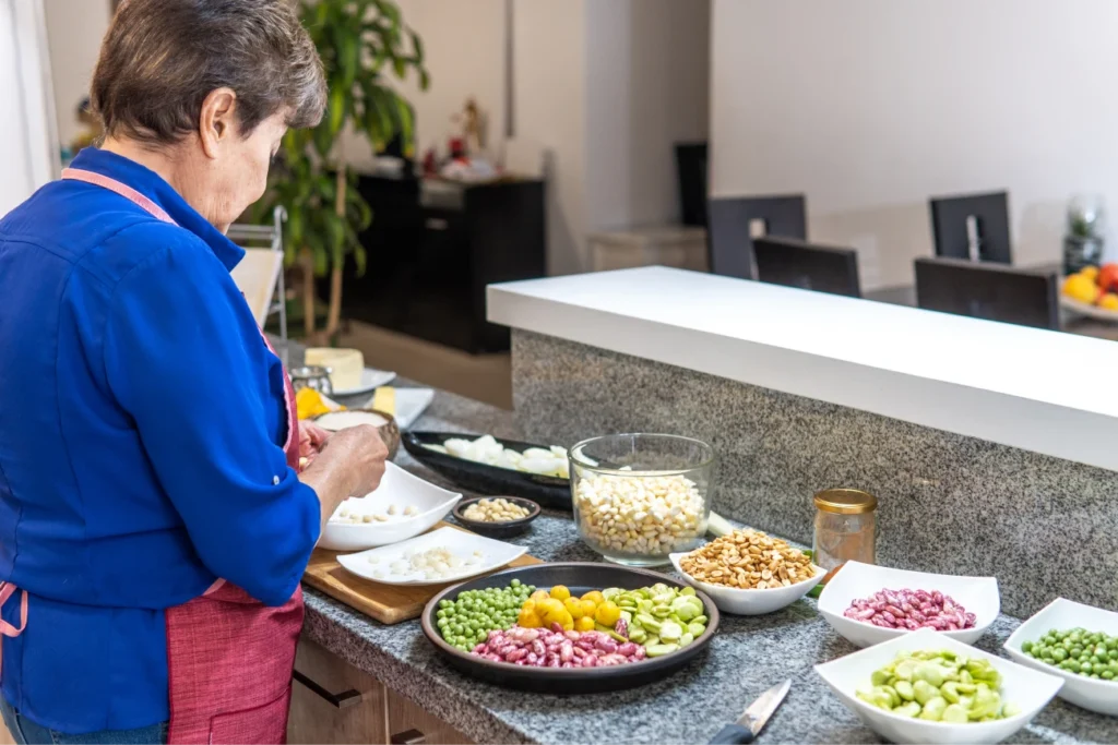 Mujer preparando legumbres y verduras en la cocina, con varios cuencos de ingredientes frescos dispuestos sobre la encimera.