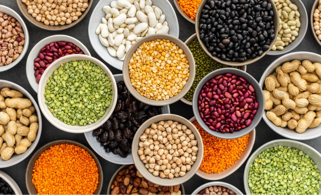 Cuencos con diferentes legumbres y semillas variadas —como lentejas, garbanzos, frijoles y guisantes— dispuestos sobre una superficie oscura.