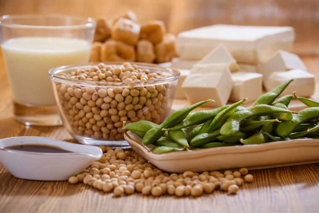 Alimentos a base de soja —como granos, edamame, tofu y leche de soja— dispuestos sobre una mesa de madera.