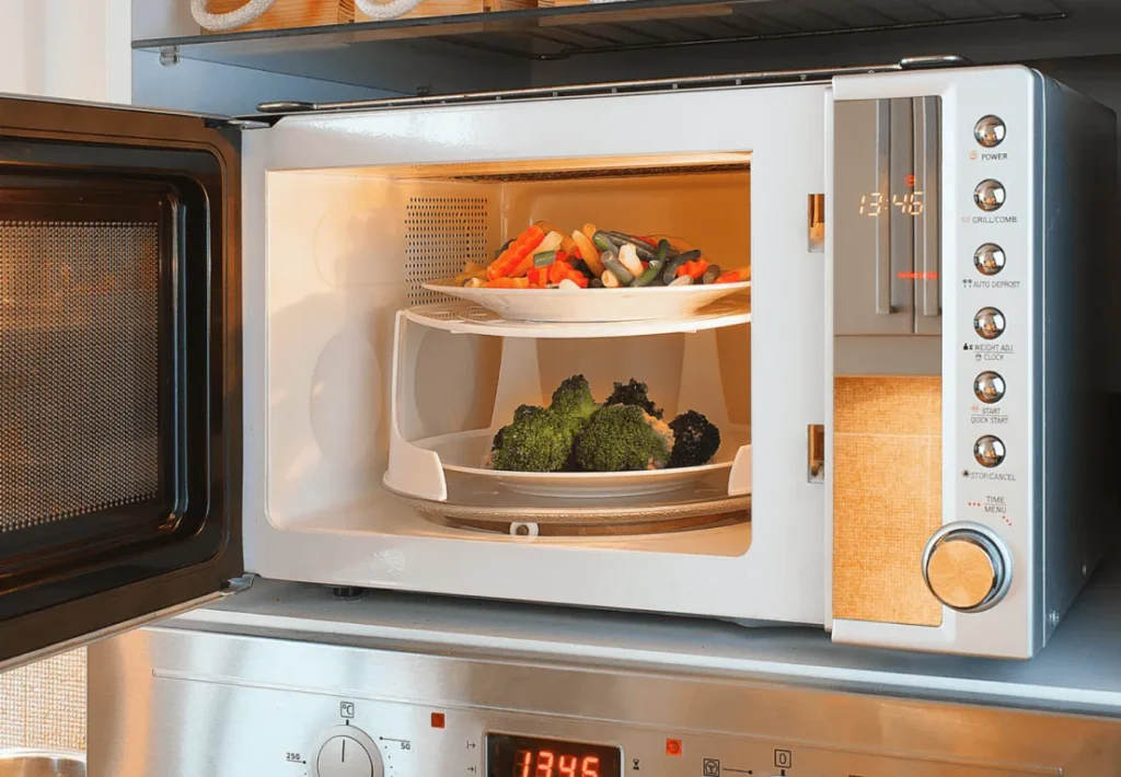 Platos con verduras dentro de un microondas abierto, listos para ser calentados o cocinados.