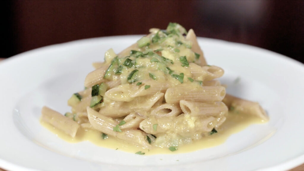 Plato de pasta integral con huevo y calabacín, cubierto con una salsa cremosa y hierbas frescas.