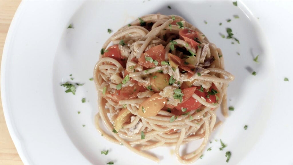 Espaguetis con anchoas, tomates y hierbas frescas, servidos en un plato blanco.