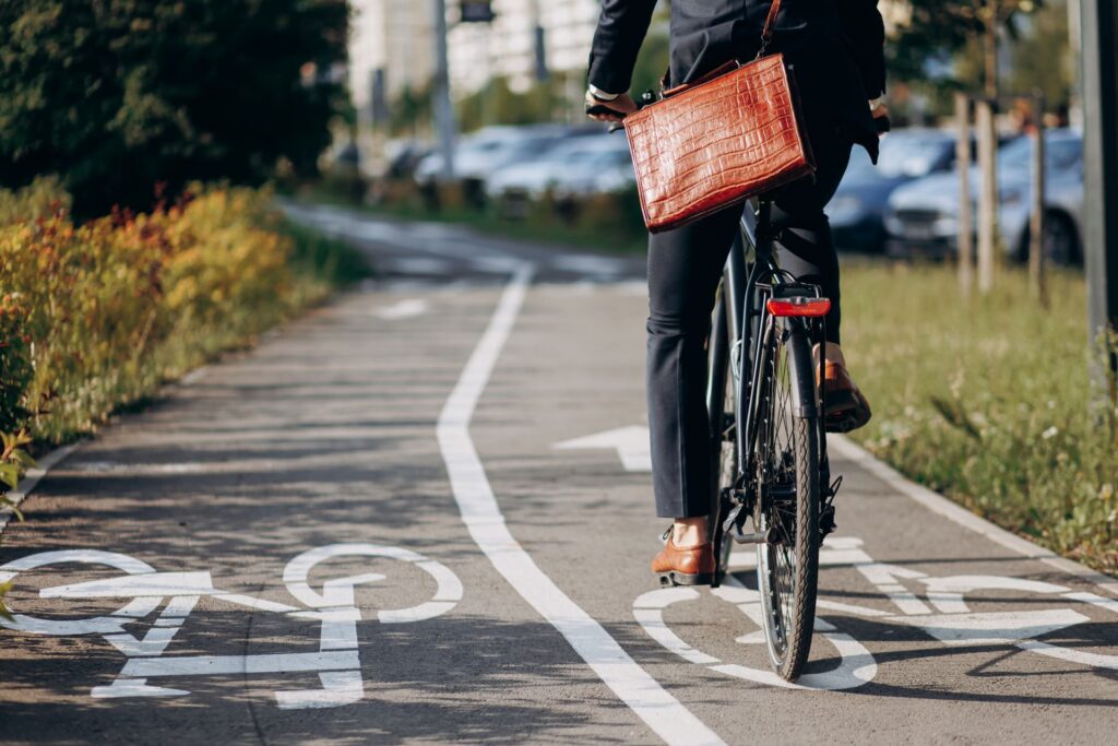Persona yendo en bicicleta por un carril bici urbano mientras se desplaza al trabajo, llevando un maletín.