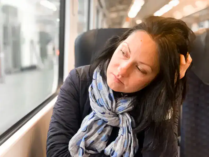 Mujer joven cansada mirando por la ventana de un tren, apoyando la cabeza en la mano